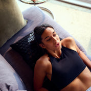 Woman in a black tank top lying on a Shakti Mat and Pillow on a couch