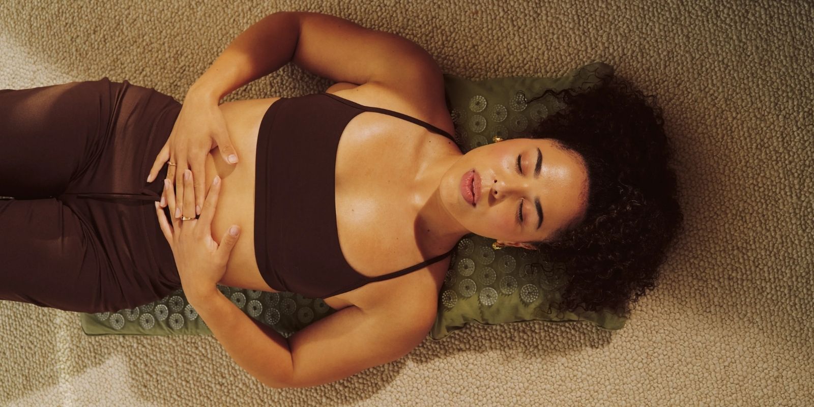 Woman laying on a Shakti Acupressure Mat and Pillow on beige carpet